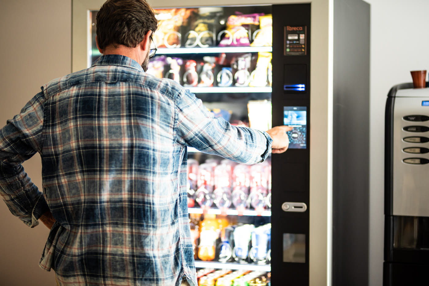 An employee selecting an item from a modern glass-front vending machine in a workplace break area
